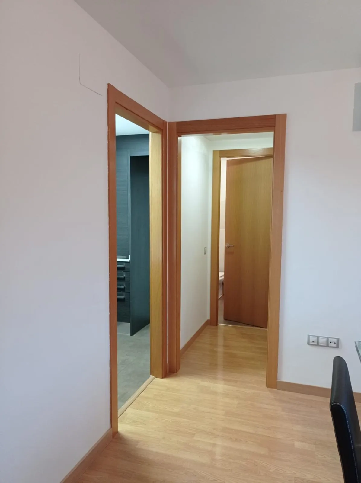Hallway with light wood floor and two open doorways showing adjacent rooms