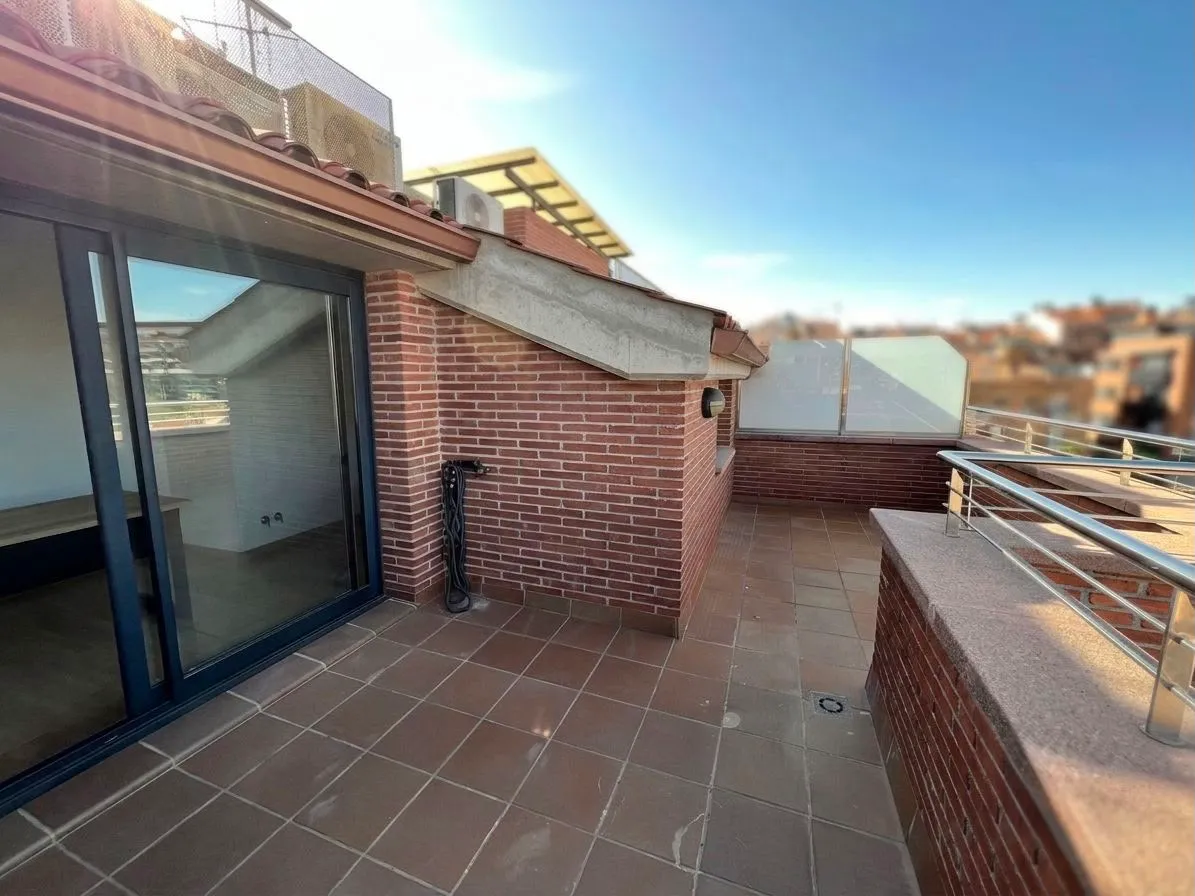 Rooftop balcony with tiled floor, brick walls, metal railing and sliding glass door leading indoors.