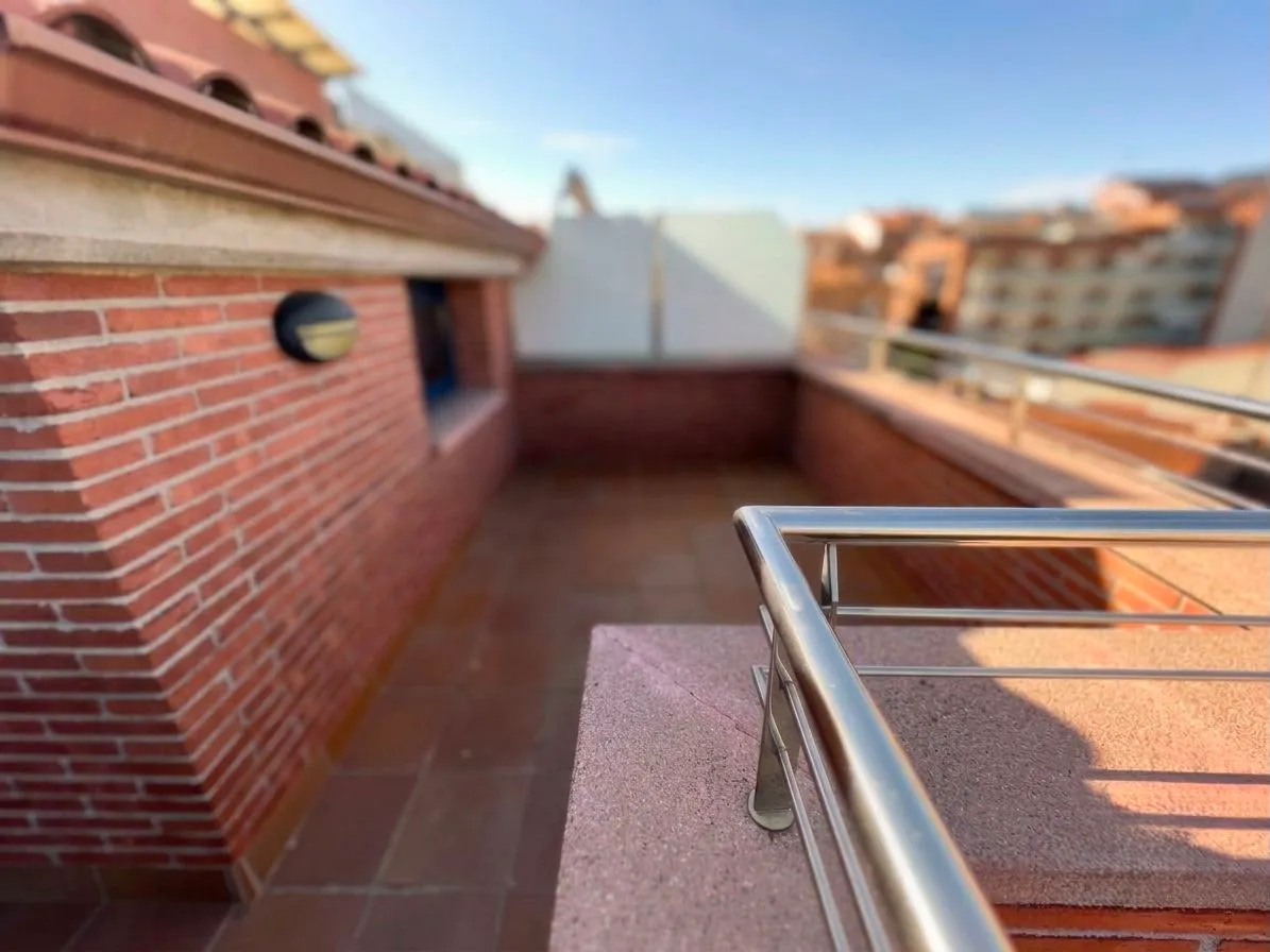 Rooftop balcony with brick walls, tiled floor and stainless-steel railing overlooking nearby buildings.