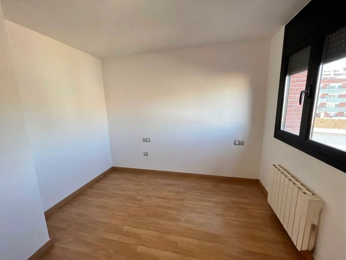 Empty room with wood-look floor, white walls, a window on the right and a wall-mounted radiator below the window.