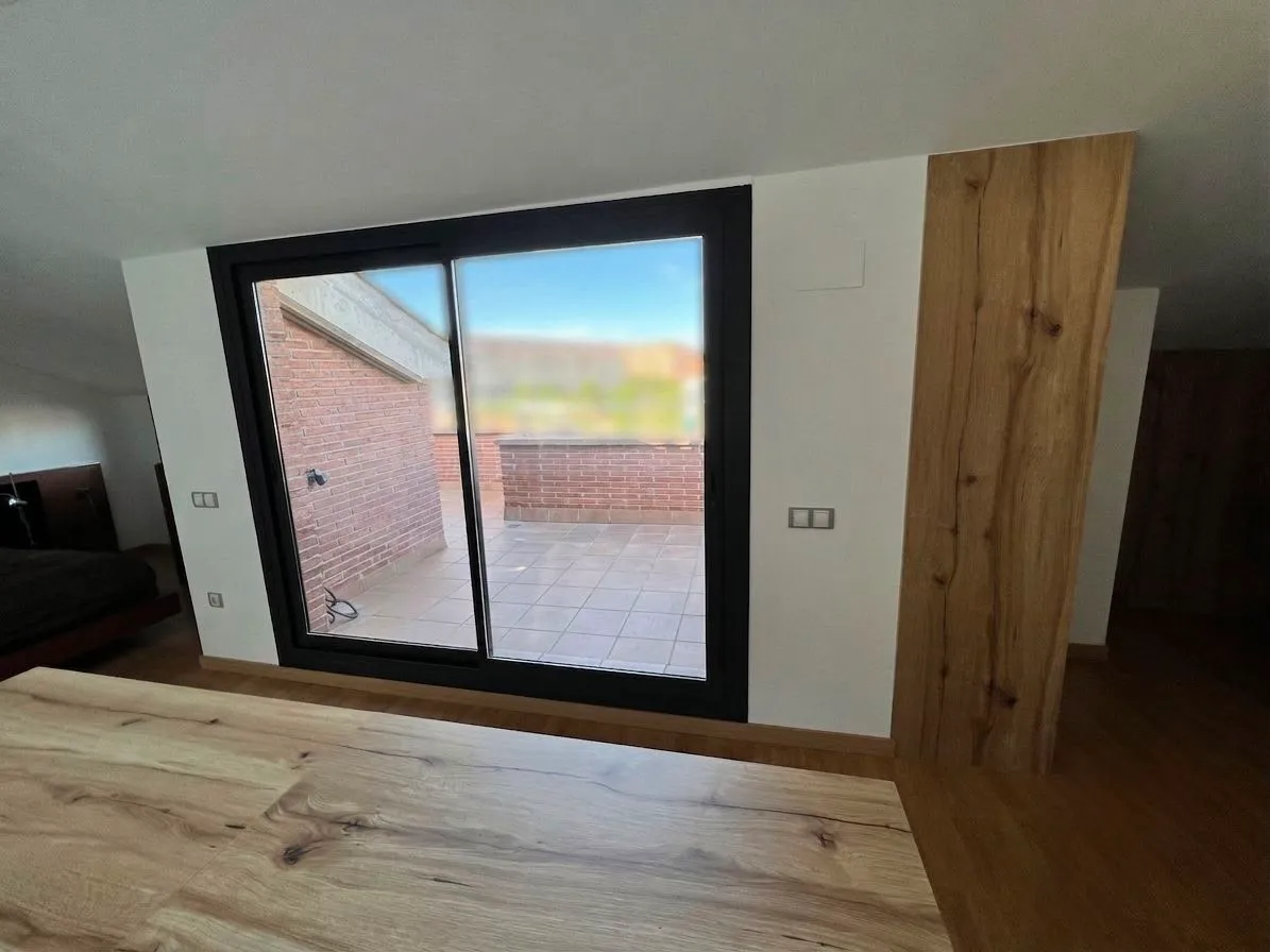 Bedroom with a large sliding glass door leading to a tiled terrace, wooden floor, and part of a bed visible at left.
