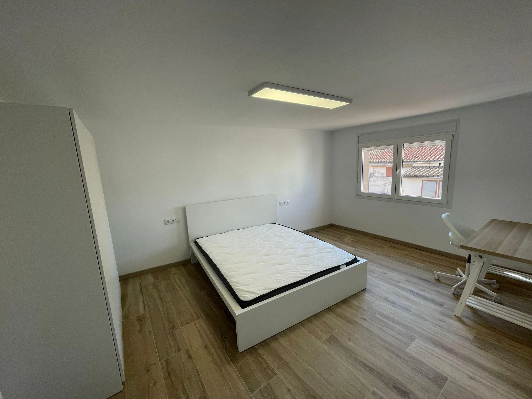 Bedroom with a single/double bed frame and mattress, window, wardrobe on left and desk with chair on right