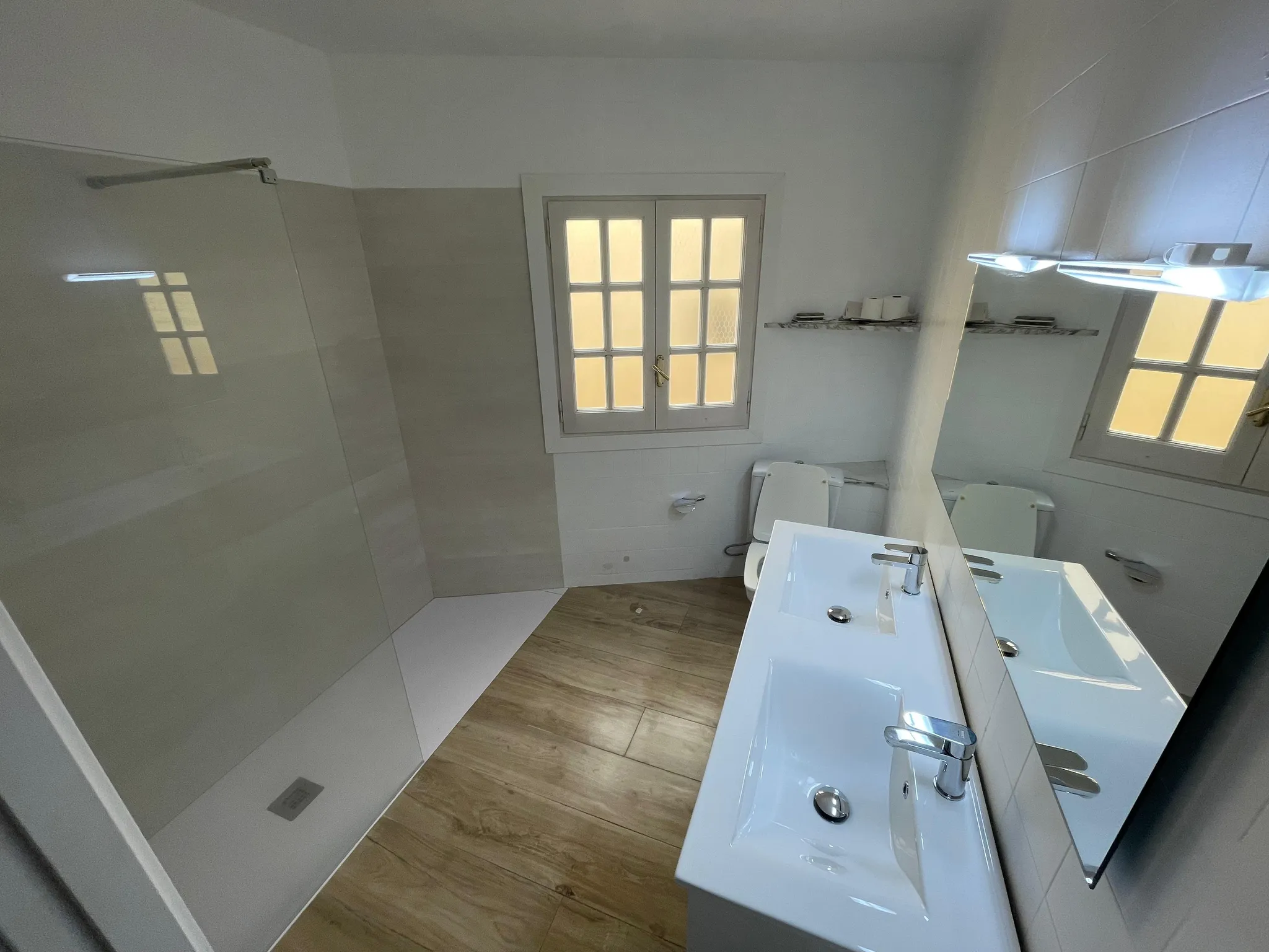 Bathroom with a double sink vanity, mirror, toilet, frosted window, and walk-in shower area