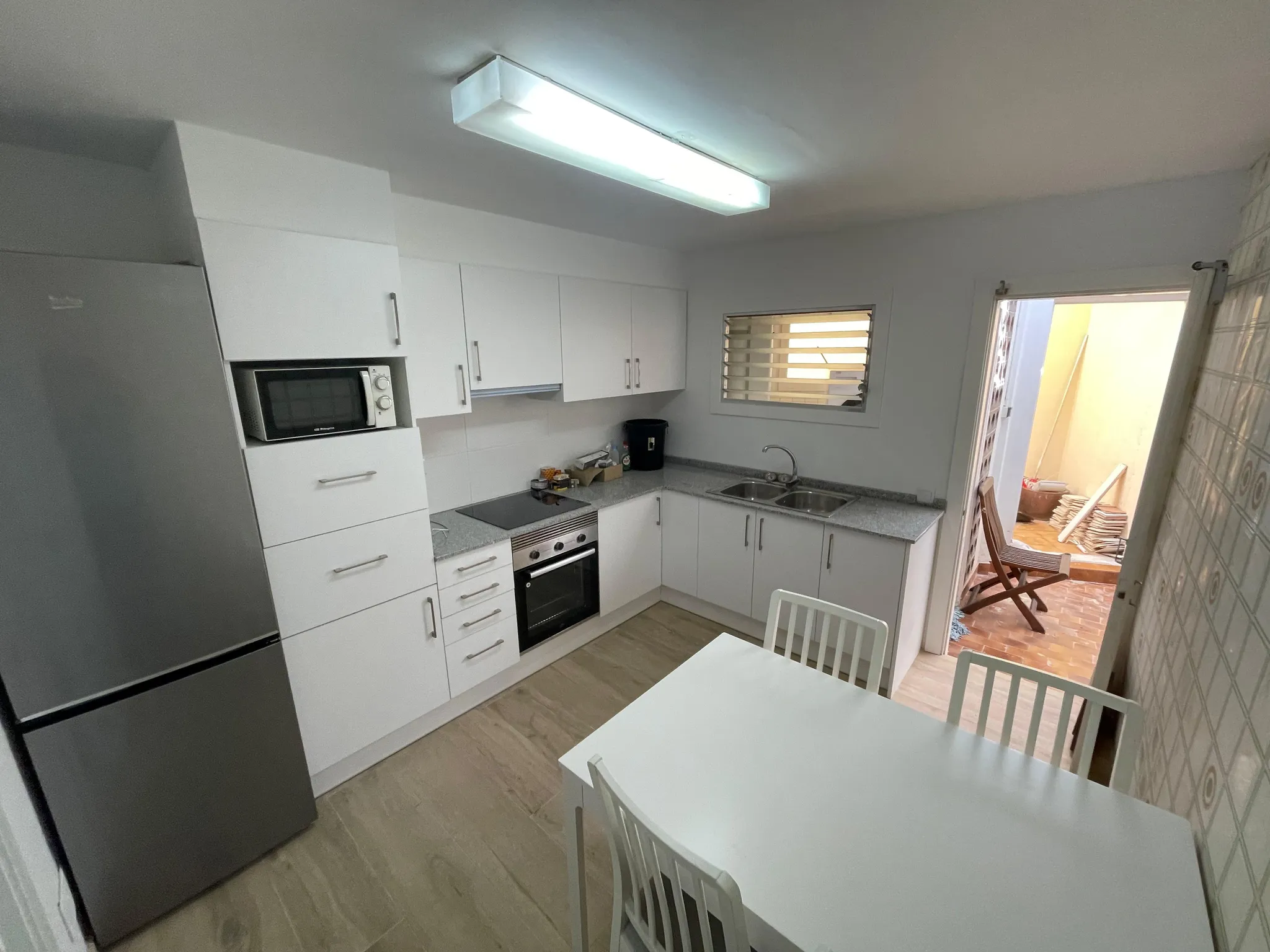 Kitchen with white cabinets, countertop, built-in oven and microwave, double sink, stainless refrigerator, and a small dining table with chairs.