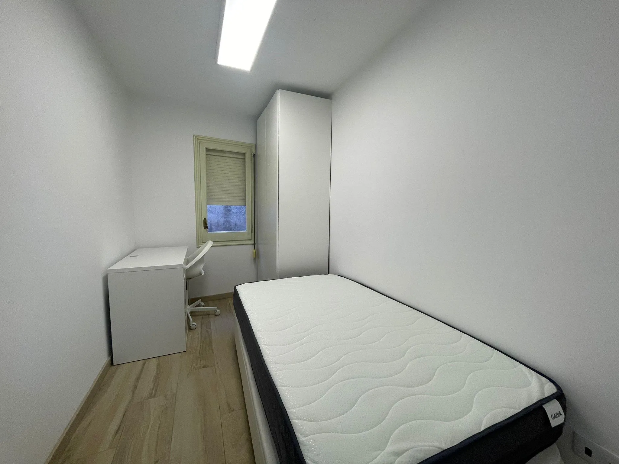 Bedroom with a single bed, wardrobe, small desk and a window with closed blind.